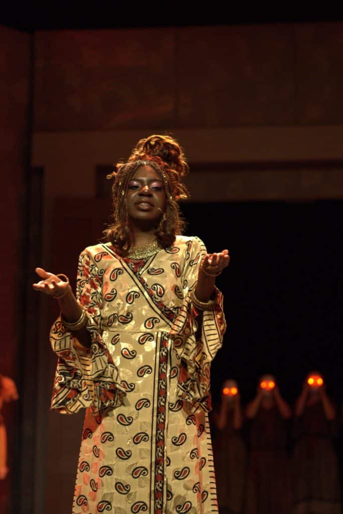 Robed Clytemnestra speaking, furies can be seen behind her