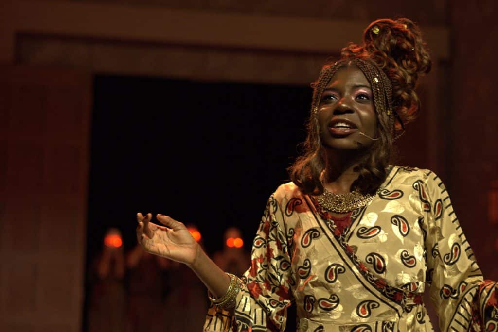 Robed Clytemnestra speaking, furies can be seen behind her